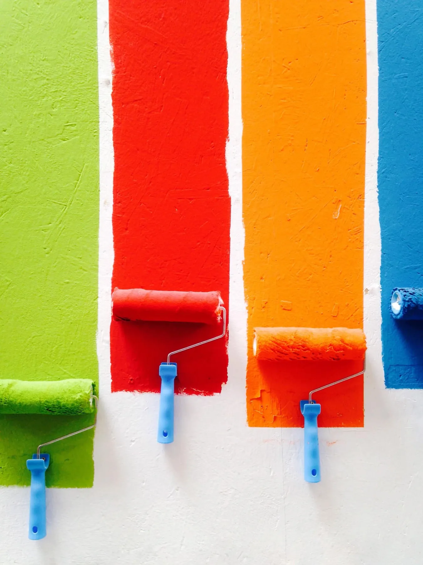Farbrollen tragen Grün, Rot, Gelb und Blau auf eine weiße Wand auf
